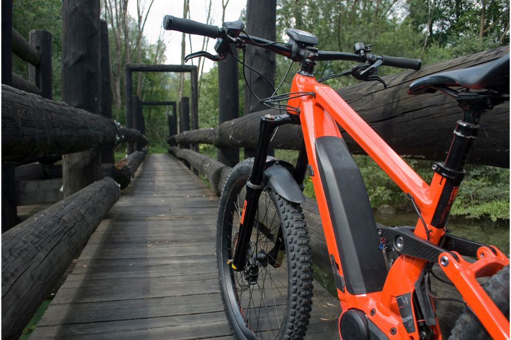  E-bike electric bicycle orange, detail from back, leaning on an old dark wooden bridge